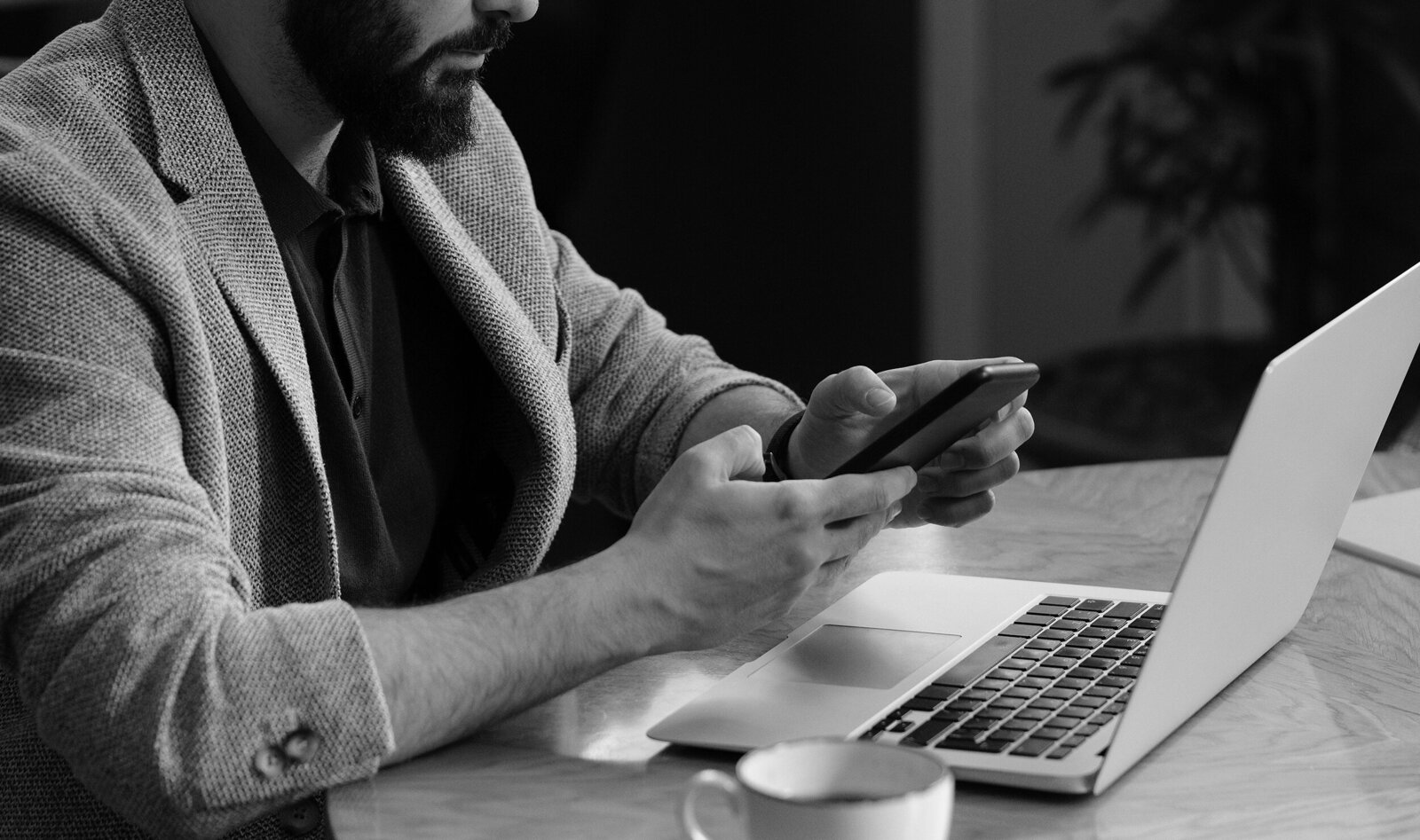 Hands working at a laptop with phone and coffee